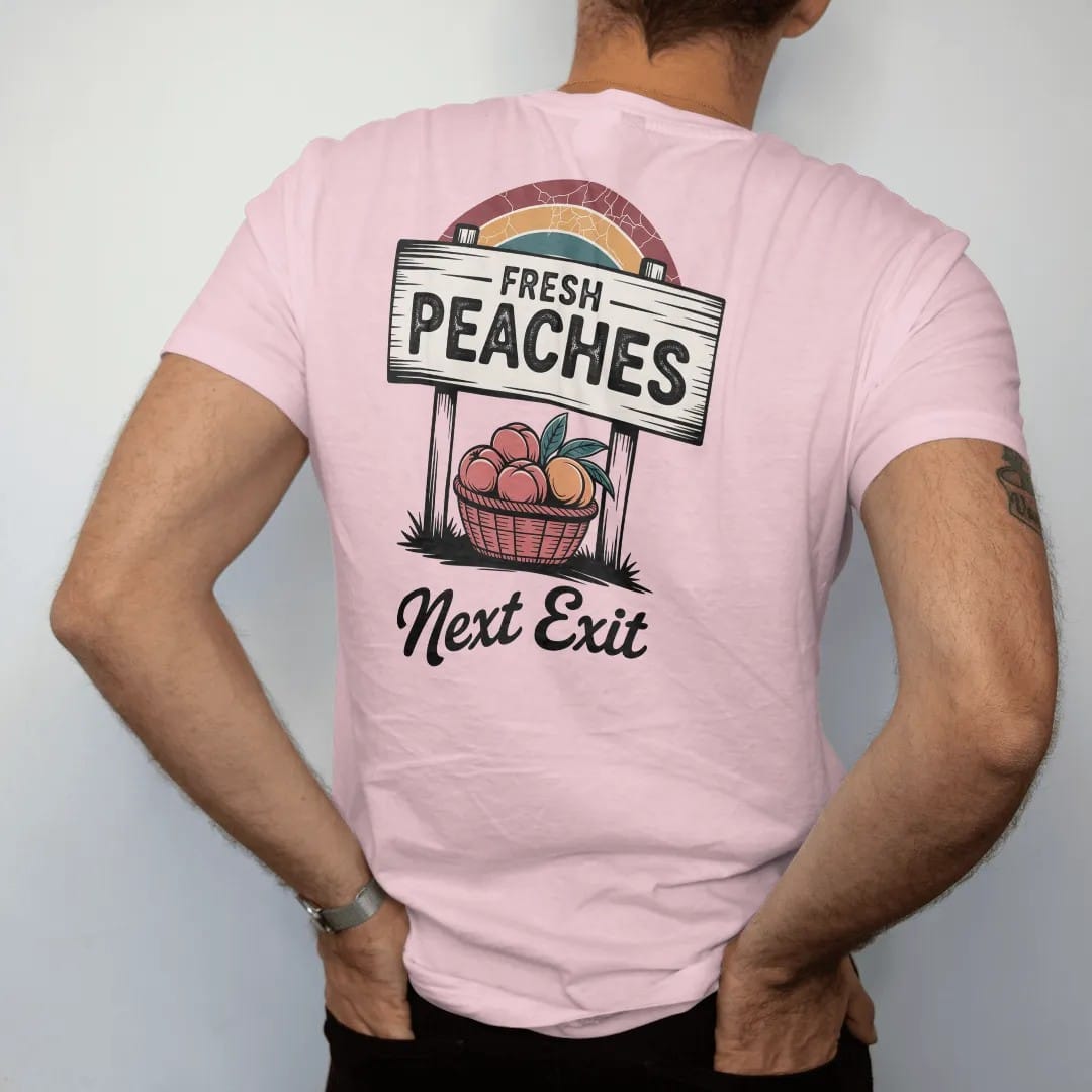 Man wearing a Blossom tee, seen from the back: a roadside produce sign over a basket of ripe peaches, with "FRESH PEACHES" and "NEXT EXIT" in chunky 70s lettering and brush script, printed in faded, cracked brown, rust red, mustard and dusty teal…