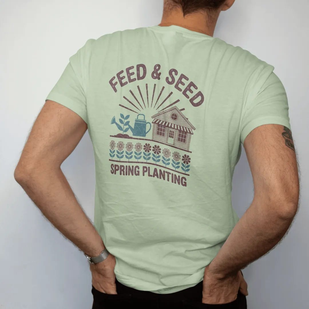 Man wearing a Light Green tee, seen from the back: a seed-packet design with seedlings, a watering can and a farm store, with "FEED & SEED" and "SPRING PLANTING" in chunky 70s lettering and small 70s caps, printed in faded, cracked brown, rust red,…