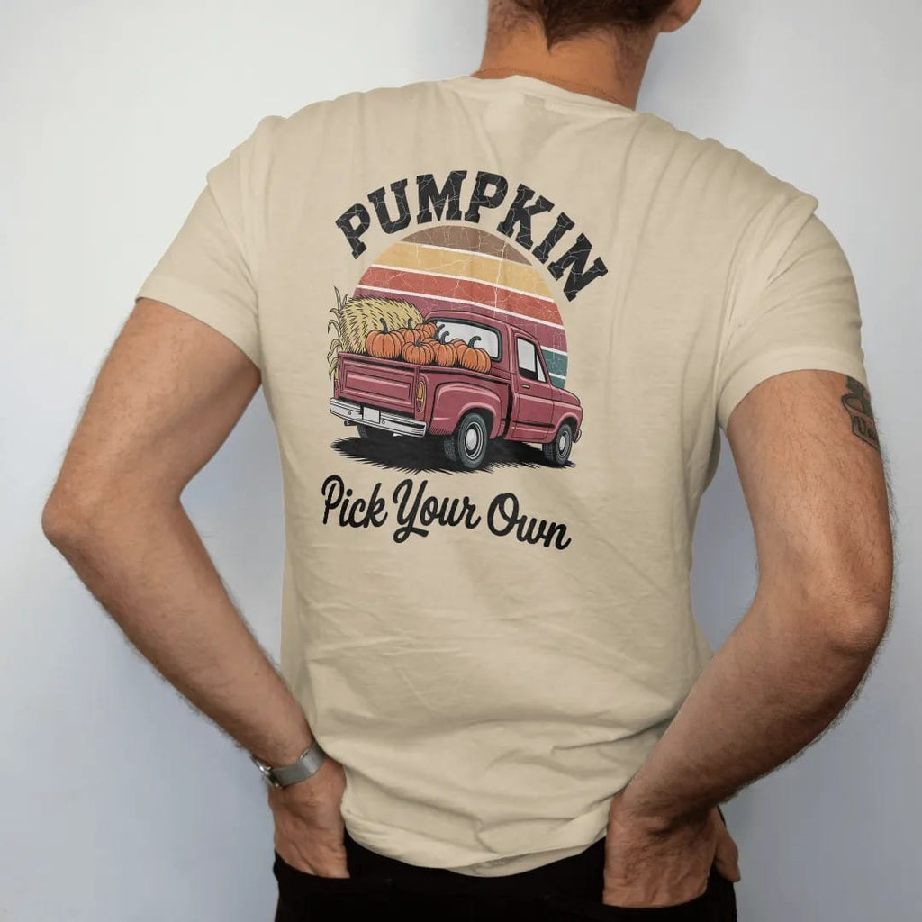 Man wearing a Sandstone tee, seen from the back: an old pickup truck bed loaded with pumpkins beside hay and corn stalks, with "PUMPKIN PATCH" and "PICK YOUR OWN" in chunky 70s lettering and brush script, printed in faded, cracked brown, rust red,…