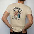 Man wearing a Sandstone tee, seen from the back: an old hardware store sign with crossed hammer and wrench, with "HARDWARE" and "NUTS · BOLTS · ADVICE" in chunky 70s lettering and small 70s caps, printed in faded, cracked brown, rust red, mustard…