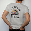 Man wearing a Granite tee, seen from the back: an old rounded pickup with rusty fenders and faded paint, with "IT'S NOT RUST" and "IT'S PATINA" in chunky 70s lettering and small 70s caps, printed in faded, cracked brown, rust red, mustard and dusty…