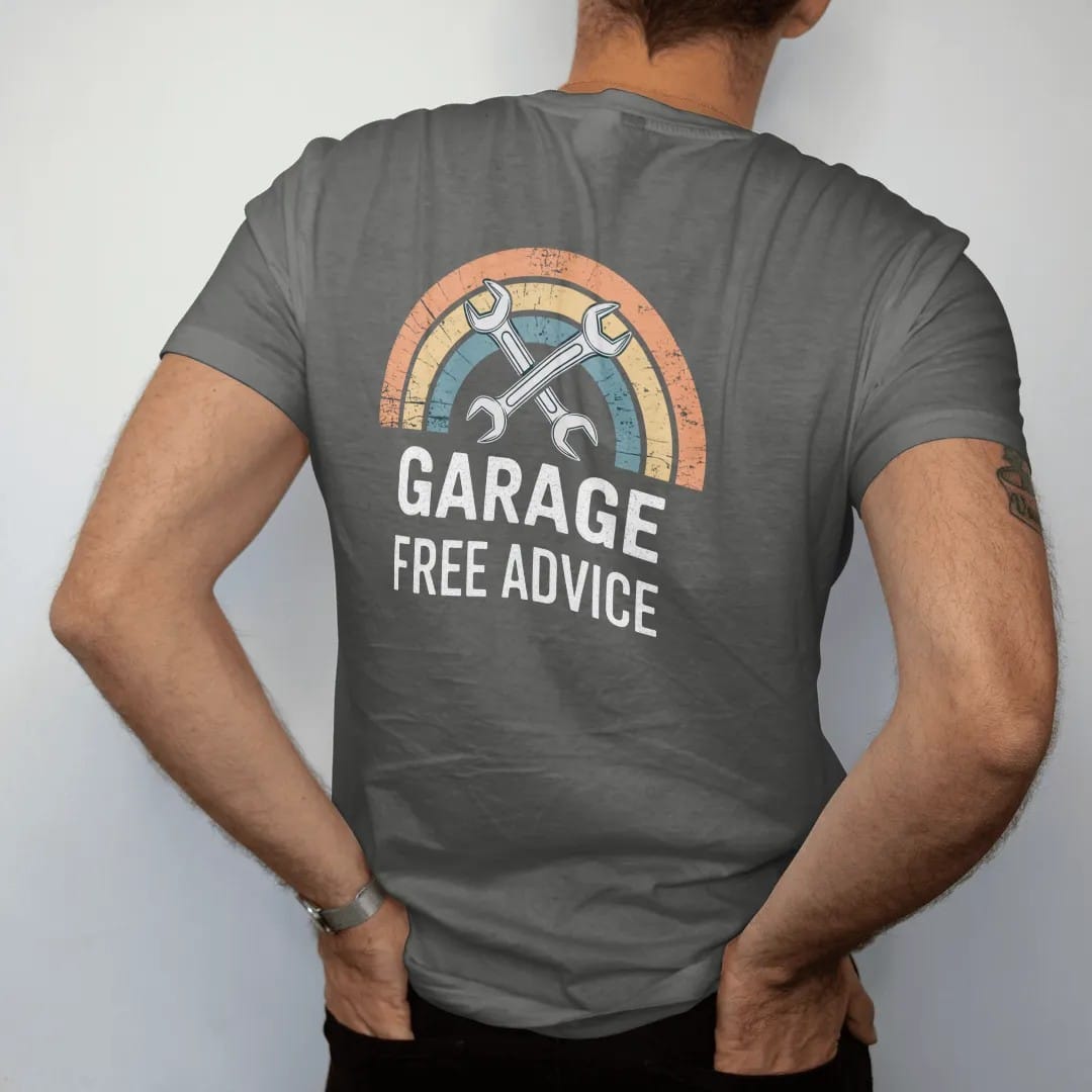 Man wearing a Pepper tee, seen from the back: an enamel garage badge with crossed wrenches and a car lift, with "DAD'S GARAGE" and "FREE ADVICE" in chunky 70s lettering and small 70s caps, printed in faded, cracked cream, mustard, burnt orange and…