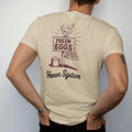 Man wearing a Sandstone tee, seen from the back: a hand-painted egg sign on a fence post with a chicken on top, with "FRESH EGGS" and "HONOR SYSTEM" in chunky 70s lettering and brush script, printed in faded, cracked brown, rust red, mustard and…