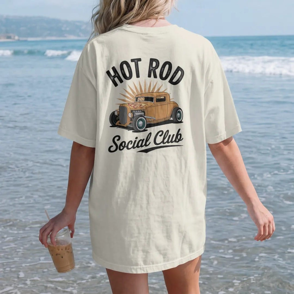 Woman on the beach in a Ivory tee, back view: a chopped hot rod coupe with hood flames and pinstripes, with "HOT ROD" and "SOCIAL CLUB" in chunky 70s lettering and brush script, printed in faded, cracked cream, mustard, burnt orange and dusty teal…