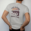Man wearing a Granite tee, seen from the back: an old general store facade with a candy jar and gumball machine, with "FIVE & DIME" and "GENERAL STORE" in chunky 70s lettering and small 70s caps, printed in faded, cracked brown, rust red, mustard…