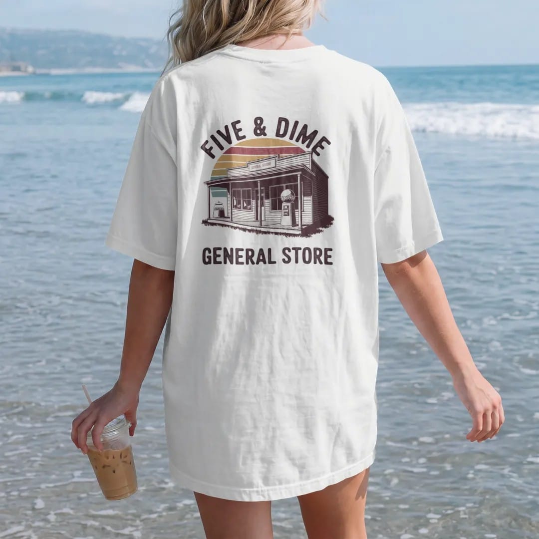 Woman on the beach in a White tee, back view: an old general store facade with a candy jar and gumball machine, with "FIVE & DIME" and "GENERAL STORE" in chunky 70s lettering and small 70s caps, printed in faded, cracked brown, rust red, mustard…