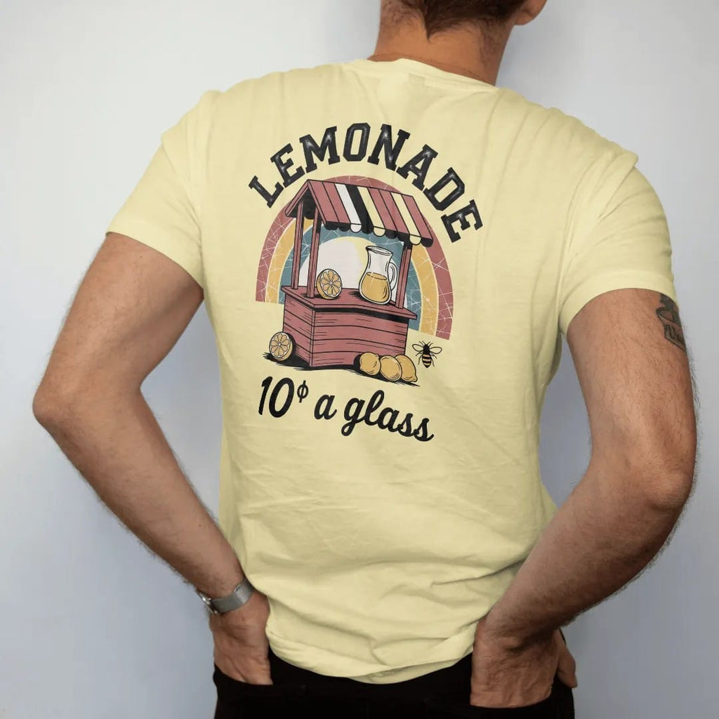 Man wearing a Butter tee, seen from the back: a wooden lemonade stand with a striped sign, pitcher and lemons, with "LEMONADE" and "10¢ A GLASS" in chunky 70s lettering and brush script, printed in faded, cracked brown, rust red, mustard and dusty…