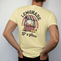 Man wearing a Butter tee, seen from the back: a wooden lemonade stand with a striped sign, pitcher and lemons, with "LEMONADE" and "10¢ A GLASS" in chunky 70s lettering and brush script, printed in faded, cracked brown, rust red, mustard and dusty…