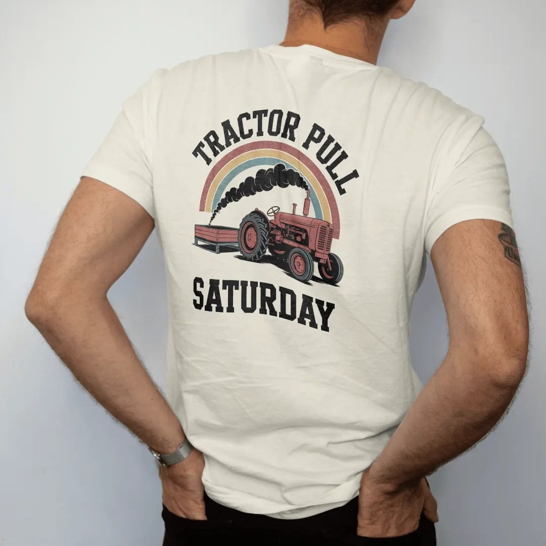 Man wearing a Ivory tee, seen from the back: an old farm tractor rearing up pulling a heavy sled, with "TRACTOR PULL" and "SATURDAY" in chunky 70s lettering and small 70s caps, printed in faded, cracked brown, rust red, mustard and dusty teal over…