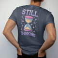 Man wearing a Midnight tee, seen from the back: a giant pixel hourglass cursor with falling sand pixels, with "STILL" and "THINKING" in liquid-chrome bubble letters and small pixel type, printed in glossy chrome silver, baby blue, bubblegum pink…