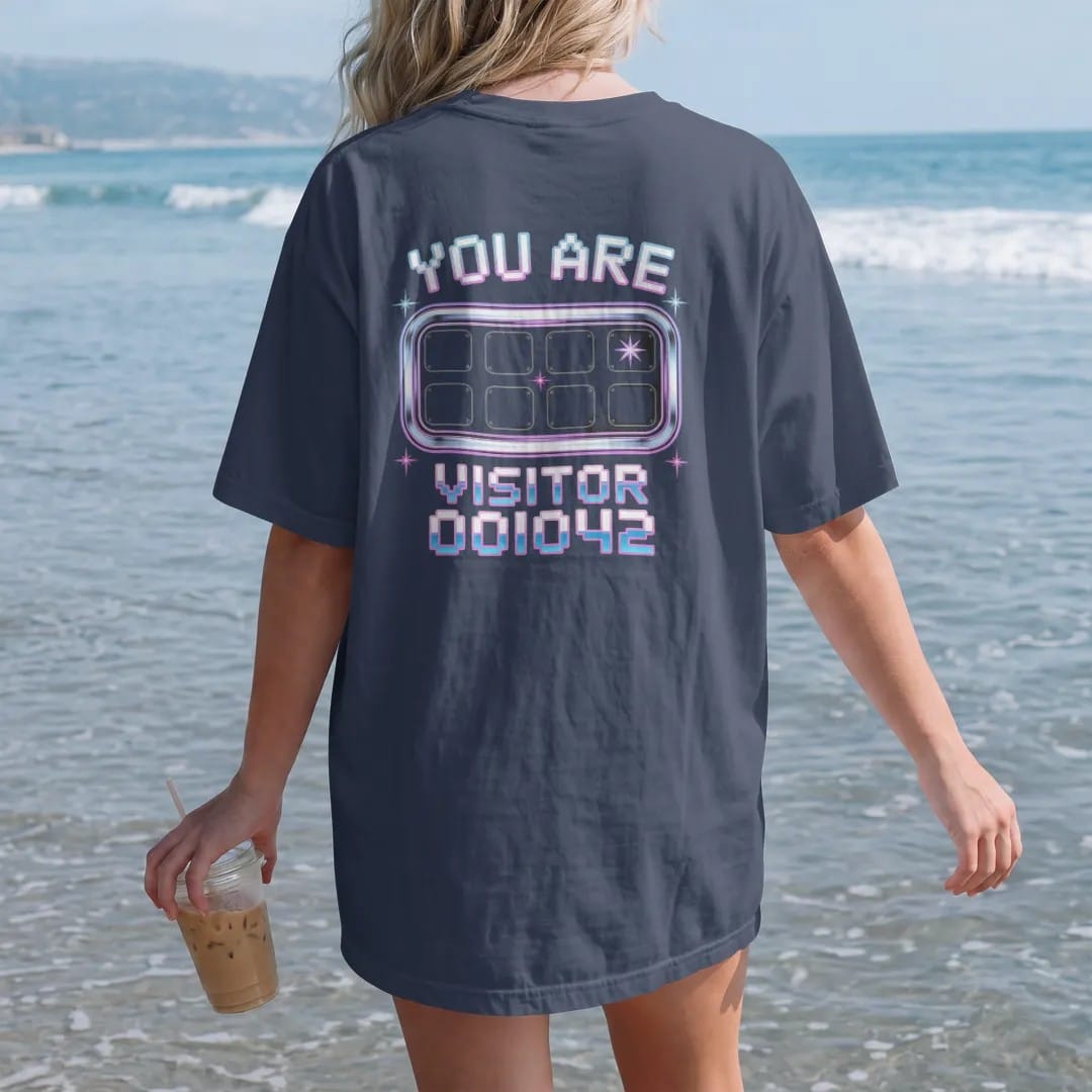 Woman on the beach in a Navy tee, back view: an odometer-style website hit counter with sparkles, with "YOU ARE" and "VISITOR 000042" in liquid-chrome bubble letters and small pixel type, printed in glossy gunmetal chrome, cobalt, hot magenta and…