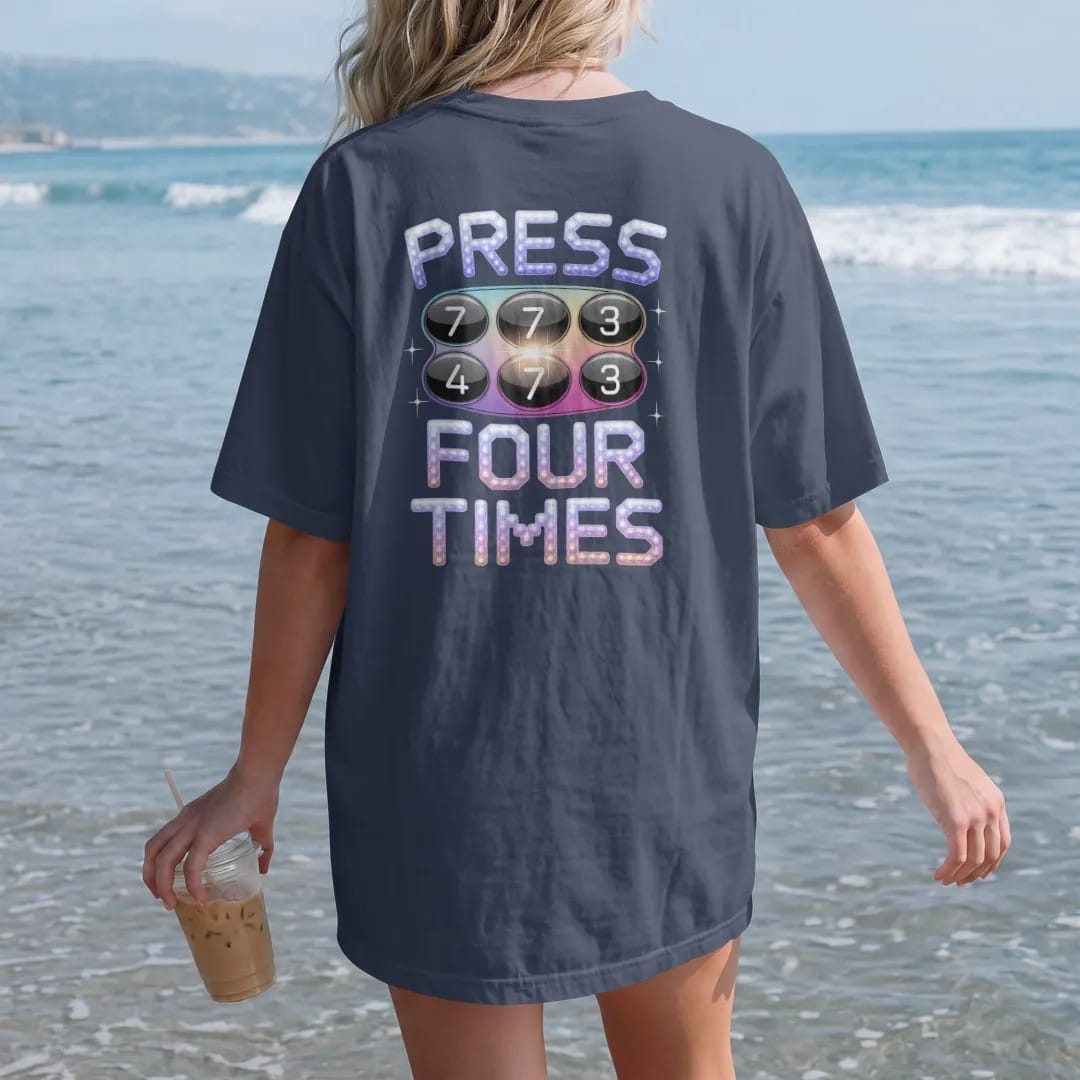 Woman on the beach in a Navy tee, back view: a chunky phone keypad with the seven key glowing, with "PRESS 7" and "FOUR TIMES" in liquid-chrome bubble letters and small pixel type, printed in glossy gunmetal chrome, cobalt, hot magenta and violet…