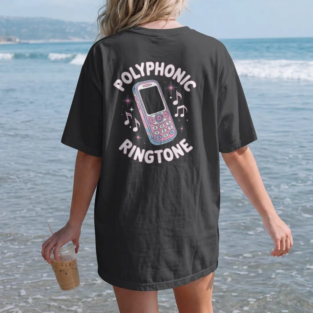 Woman on the beach in a Black tee, back view: a candy-bar cell phone ringing with pixel music notes, with "POLYPHONIC" and "RINGTONE" in liquid-chrome bubble letters and small pixel type, printed in glossy chrome silver, baby blue, bubblegum pink…
