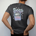 Man wearing a Black tee, seen from the back: a translucent clip-on pager with a tiny number on its screen, with "BEEP ME" in liquid-chrome bubble letters, printed in glossy gunmetal chrome, cobalt, hot magenta and violet with sparkles.
