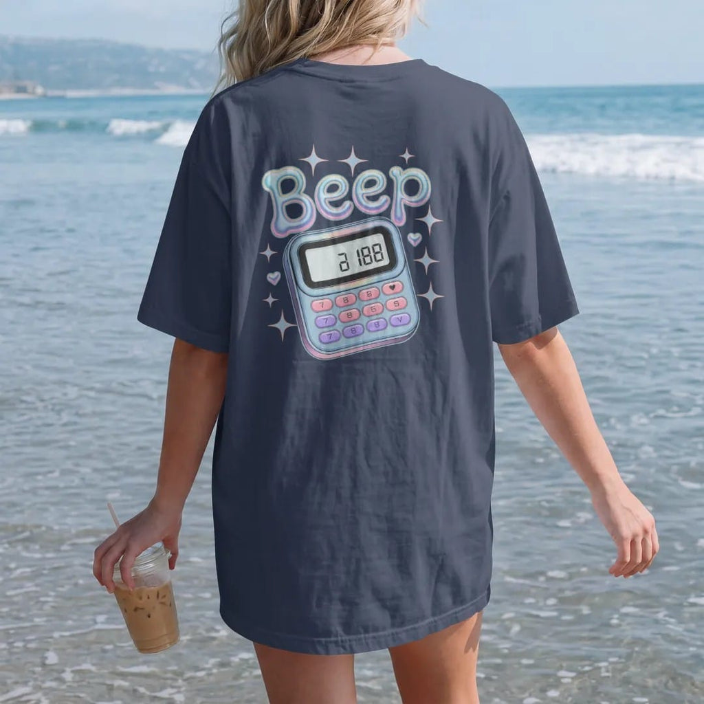 Woman on the beach in a Navy tee, back view: a translucent clip-on pager with a tiny number on its screen, with "BEEP ME" in liquid-chrome bubble letters, printed in glossy gunmetal chrome, cobalt, hot magenta and violet with sparkles.