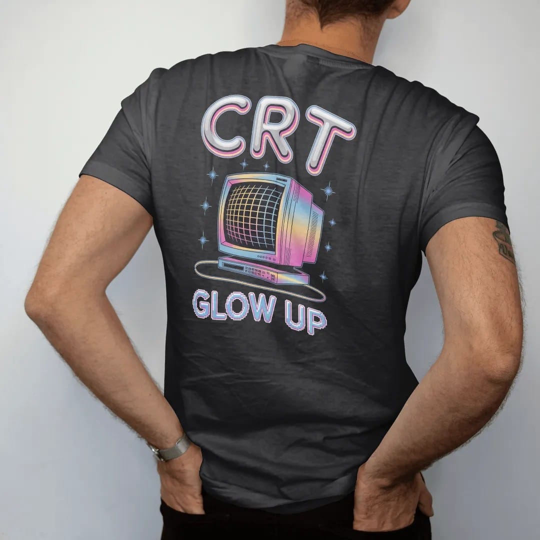 Man wearing a Black tee, seen from the back: a chunky CRT monitor with a glowing scanline screen, with "CRT" and "GLOW UP" in liquid-chrome bubble letters and small pixel type, printed in glossy chrome silver, baby blue, bubblegum pink and violet…