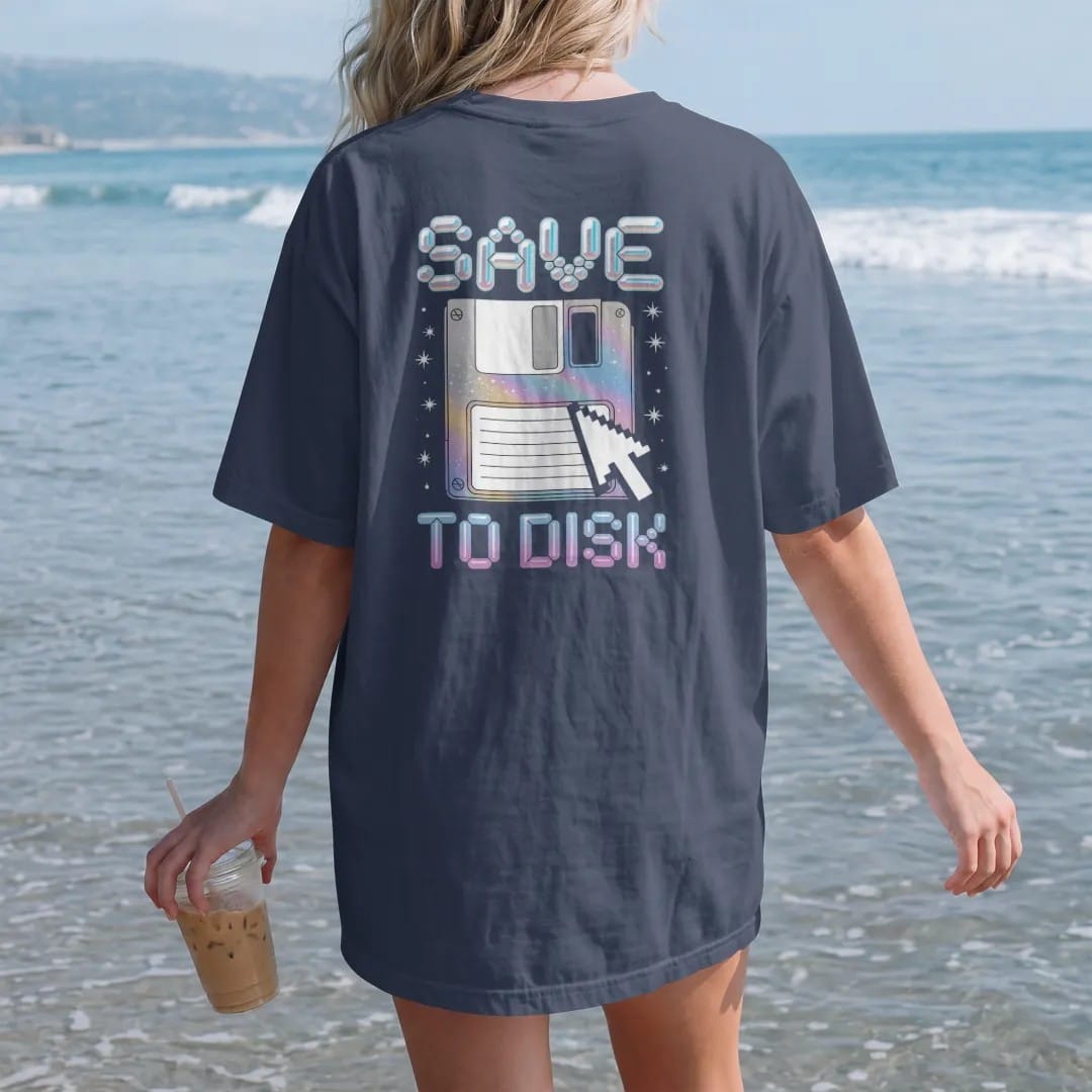 Woman on the beach in a Navy tee, back view: an oversized floppy disk with a pixel cursor clicking it, with "SAVE" and "TO DISK" in liquid-chrome bubble letters and small pixel type, printed in glossy gunmetal chrome, cobalt, hot magenta and violet…