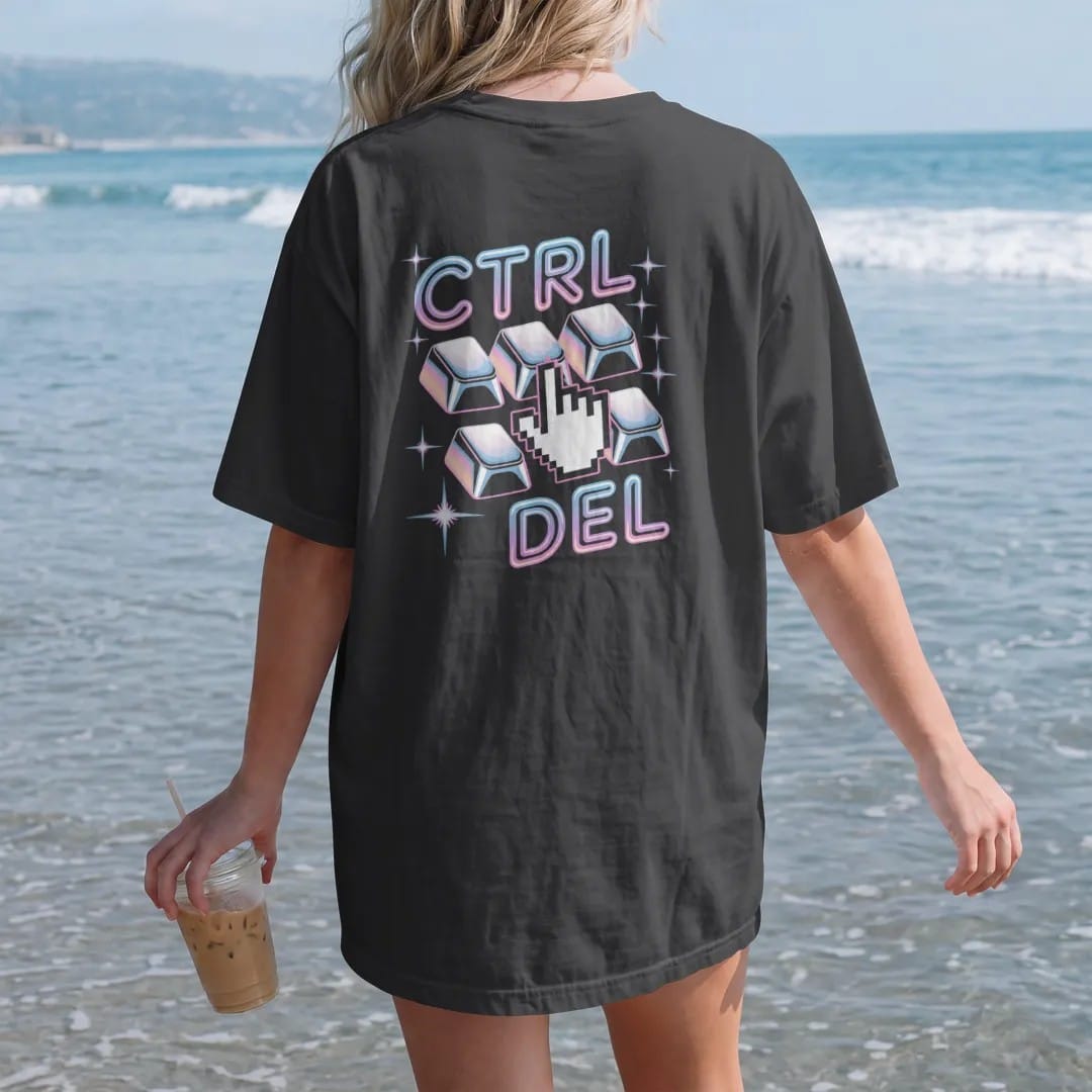 Woman on the beach in a Black tee, back view: three chunky keyboard keys pressed by a pixel hand, with "CTRL", "ALT" and "DEL" in liquid-chrome bubble letters and small pixel type, printed in glossy chrome silver, baby blue, bubblegum pink and…