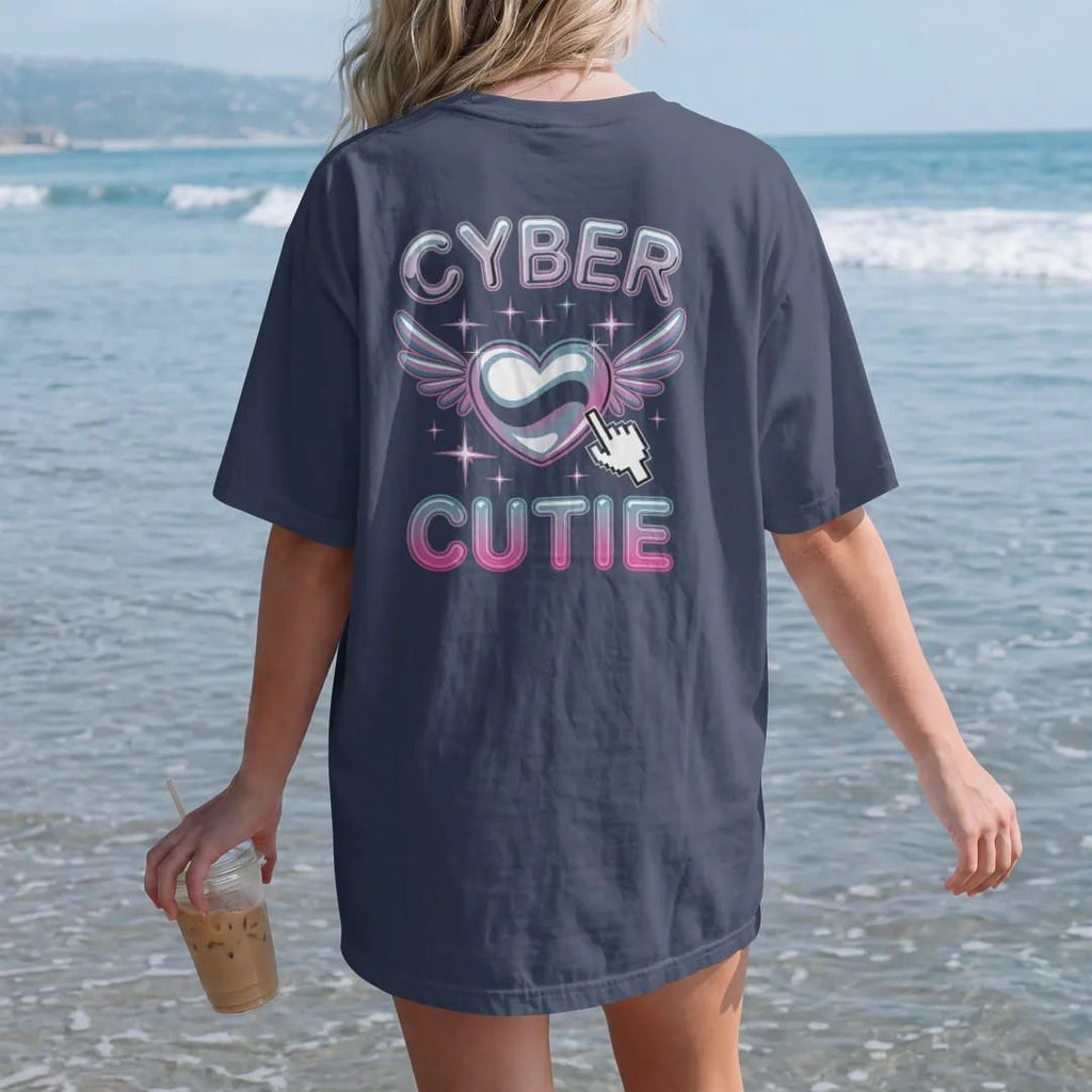 Woman on the beach in a Navy tee, back view: a winged chrome bubble heart with sparkles and a pixel cursor, with "CYBER" and "CUTIE" in liquid-chrome bubble letters and small pixel type, printed in glossy gunmetal chrome, cobalt, hot magenta and…