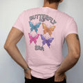Man wearing a Blossom tee, seen from the back: a row of colorful butterfly hair clips with glitter sparkles, with "BUTTERFLY CLIP" and "ERA" in liquid-chrome bubble letters and small pixel type, printed in glossy gunmetal chrome, cobalt, hot…