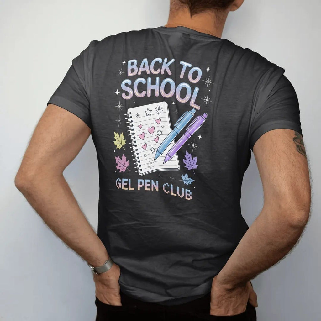 Man wearing a Black tee, seen from the back: glitter gel pens and a doodled notebook among fall leaves, with "BACK TO SCHOOL" and "GEL PEN CLUB" in liquid-chrome bubble letters and small pixel type, printed in glossy gunmetal chrome, cobalt, hot…