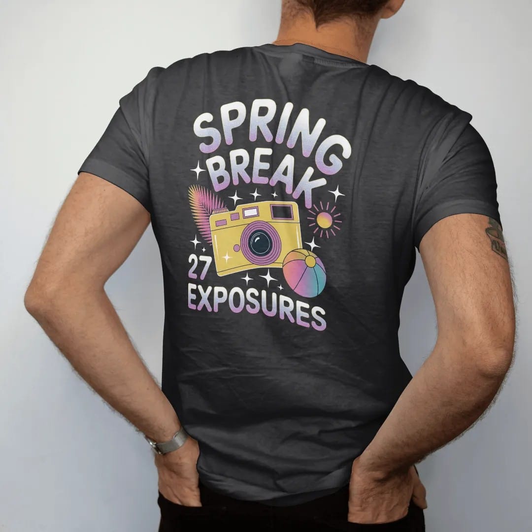Man wearing a Black tee, seen from the back: a yellow disposable camera with a flash burst and palm leaves, with "SPRING BREAK" and "27 EXPOSURES" in liquid-chrome bubble letters and small pixel type, printed in glossy gunmetal chrome, cobalt, hot…