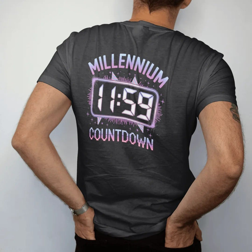 Man wearing a Black tee, seen from the back: a glowing digital clock at 11:59 with confetti and party hats, with "MILLENNIUM" and "COUNTDOWN" in liquid-chrome bubble letters and small pixel type, printed in glossy chrome silver, baby blue,…
