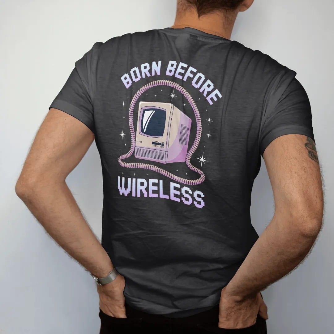Man wearing a Black tee, seen from the back: a tangled phone cord framing a beige computer tower, with "BORN BEFORE" and "WIRELESS" in liquid-chrome bubble letters and small pixel type, printed in glossy gunmetal chrome, cobalt, hot magenta and…