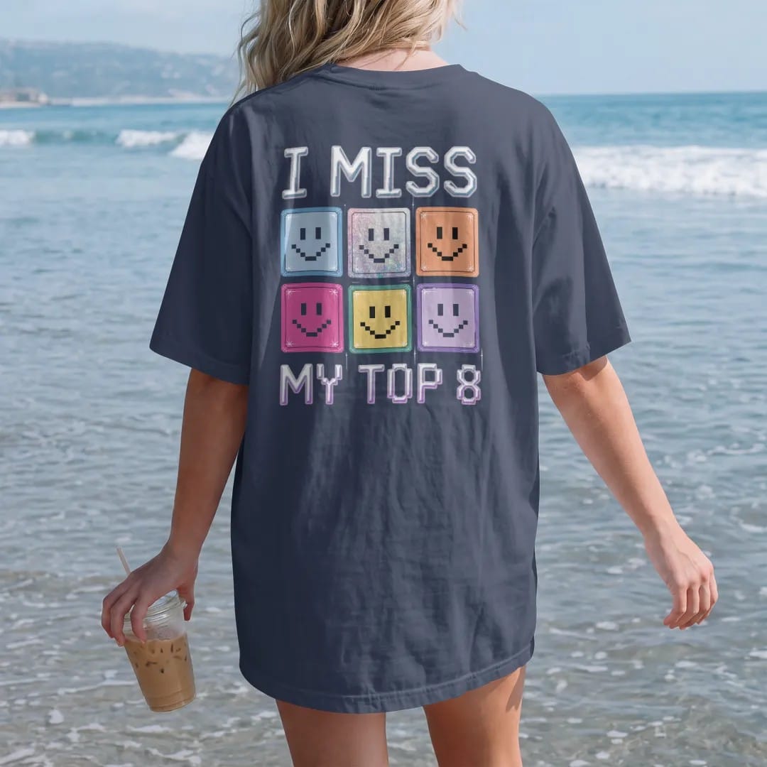 Woman on the beach in a Navy tee, back view: a grid of eight pixel smiley photo frames, with "I MISS" and "MY TOP 8" in liquid-chrome bubble letters and small pixel type, printed in glossy gunmetal chrome, cobalt, hot magenta and violet with…