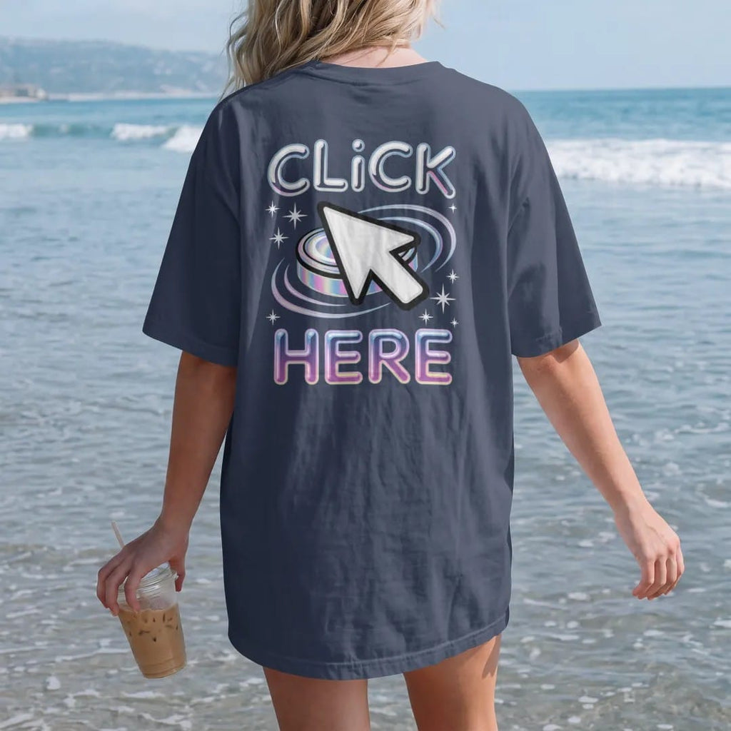 Woman on the beach in a Navy tee, back view: an oversized pixel cursor clicking a glossy beveled button, with "CLICK" and "HERE" in liquid-chrome bubble letters and small pixel type, printed in glossy chrome silver, baby blue, bubblegum pink and…