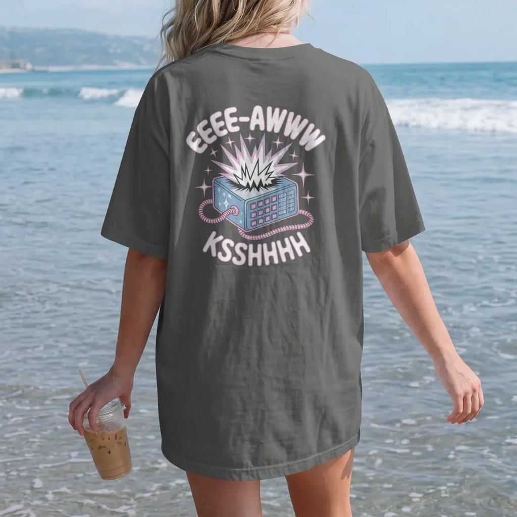 Woman on the beach in a Pepper tee, back view: a jagged sound-wave burst exploding from a modem, with "EEEE-AWWW" and "KSSHHHH" in liquid-chrome bubble letters and small pixel type, printed in glossy chrome silver, baby blue, bubblegum pink and…