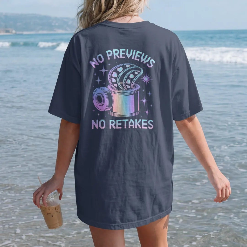 Woman on the beach in a Navy tee, back view: a roll of film unspooling with heart and star frames, with "NO PREVIEWS" and "NO RETAKES" in liquid-chrome bubble letters and small pixel type, printed in glossy gunmetal chrome, cobalt, hot magenta and…