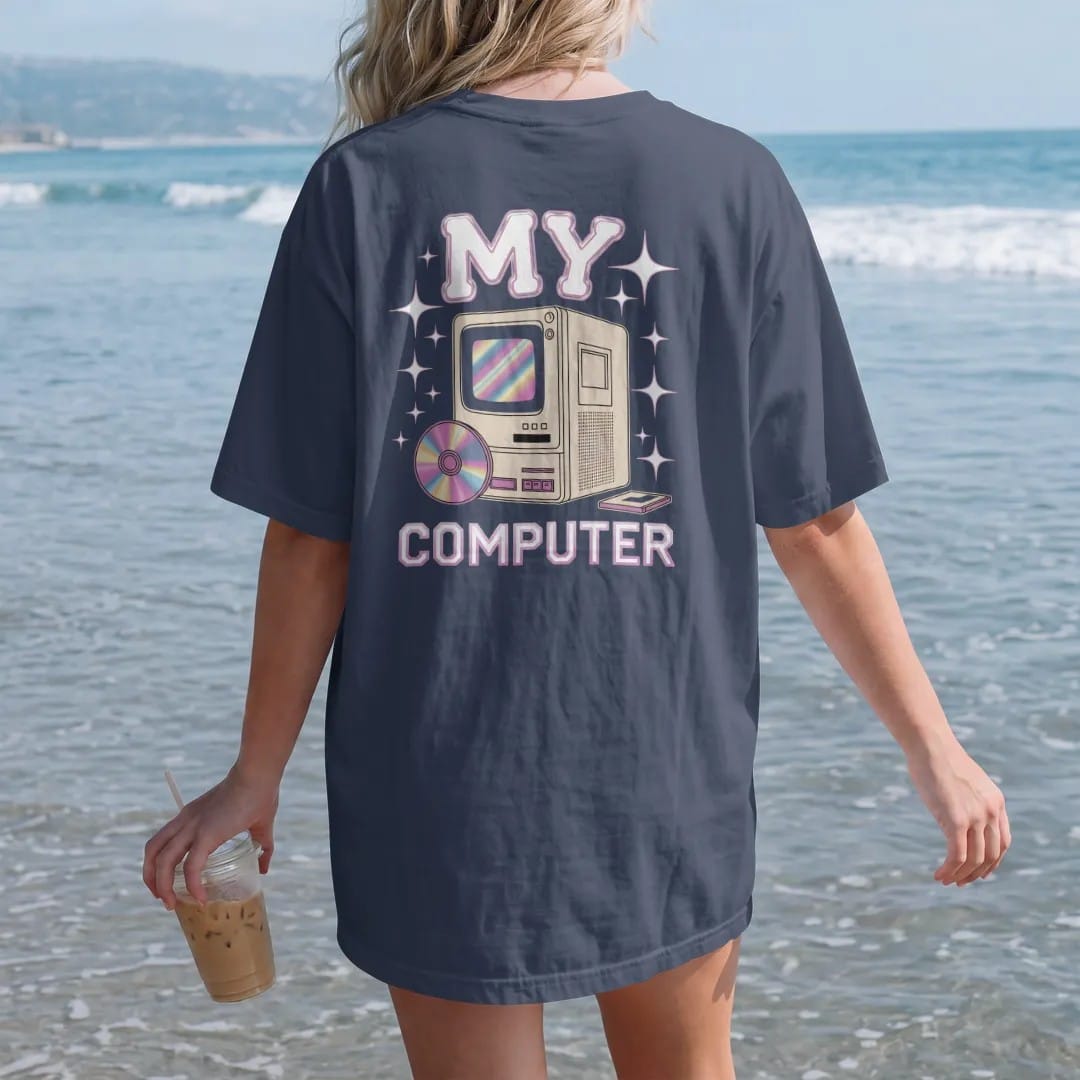 Woman on the beach in a Navy tee, back view: a chunky beige desktop tower with an open disc tray, with "MY" and "COMPUTER" in liquid-chrome bubble letters and small pixel type, printed in glossy gunmetal chrome, cobalt, hot magenta and violet with…