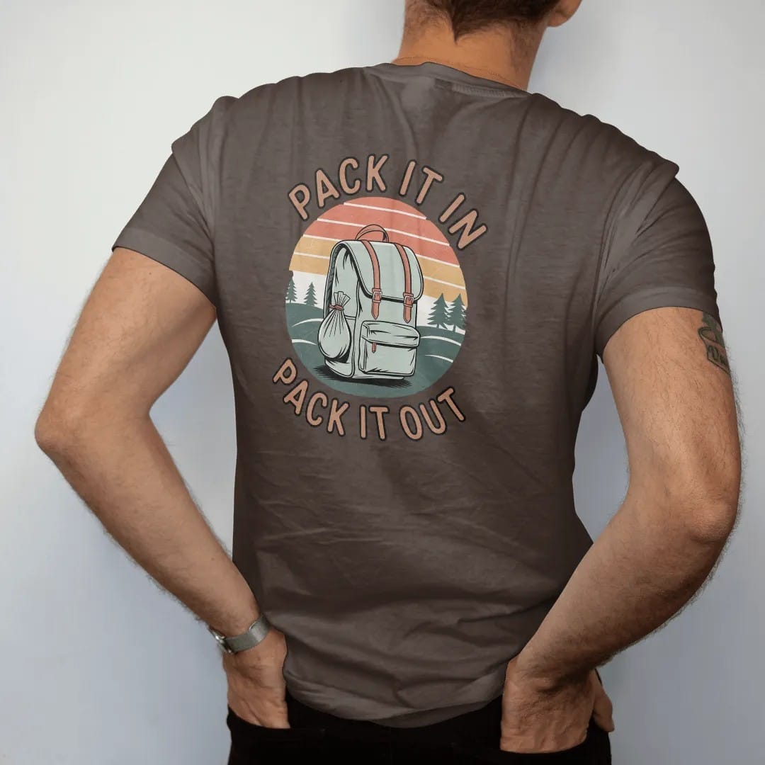 Man wearing a Espresso tee, seen from the back: a loaded backpack with a small trash bag tied on, rolling hills behind, stacked text, faded 70s park-souvenir style, lettered "PACK IT IN / PACK IT OUT" in chunky rounded 70s letters with a drop…