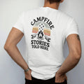 Man wearing a White tee, seen from the back: a crackling campfire with sparks rising into stars and two logs as benches, arched header and small sign below, faded 70s park-souvenir style, lettered "CAMPFIRE STORIES / TOLD HERE" in chunky rounded…