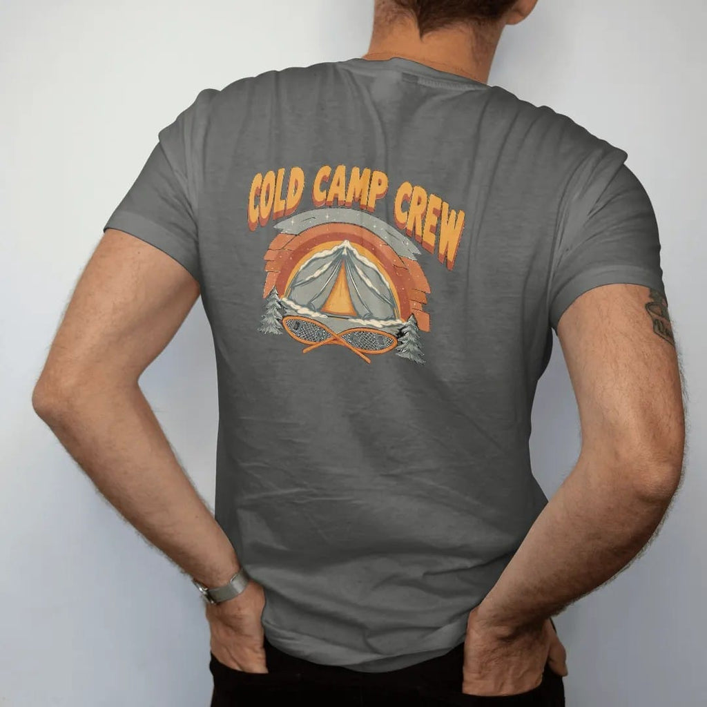 Man wearing a Pepper tee, seen from the back: a snow-covered tent glowing from within under a starry winter sky with crossed snowshoes below, faded 70s park-souvenir style, lettered "COLD CAMP CREW" in chunky rounded 70s letters with a drop shadow,…