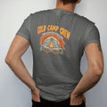 Man wearing a Pepper tee, seen from the back: a snow-covered tent glowing from within under a starry winter sky with crossed snowshoes below, faded 70s park-souvenir style, lettered "COLD CAMP CREW" in chunky rounded 70s letters with a drop shadow,…