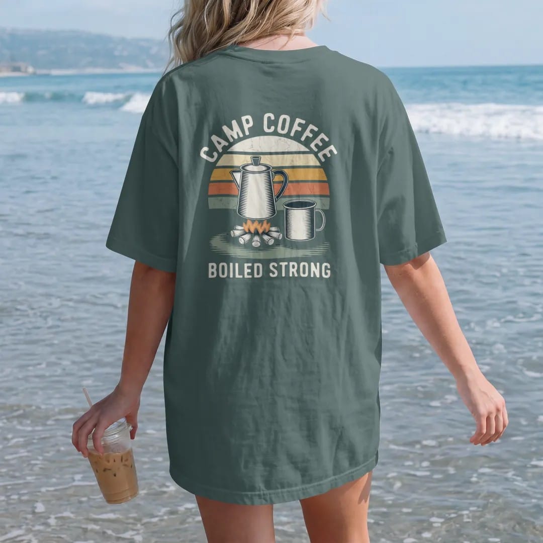 Woman on the beach in a Blue Spruce tee, back view: an enamel percolator steaming over a small campfire with a tin mug beside it, label-style layout, faded 70s park-souvenir style, lettered "CAMP COFFEE / BOILED STRONG" in chunky rounded 70s…