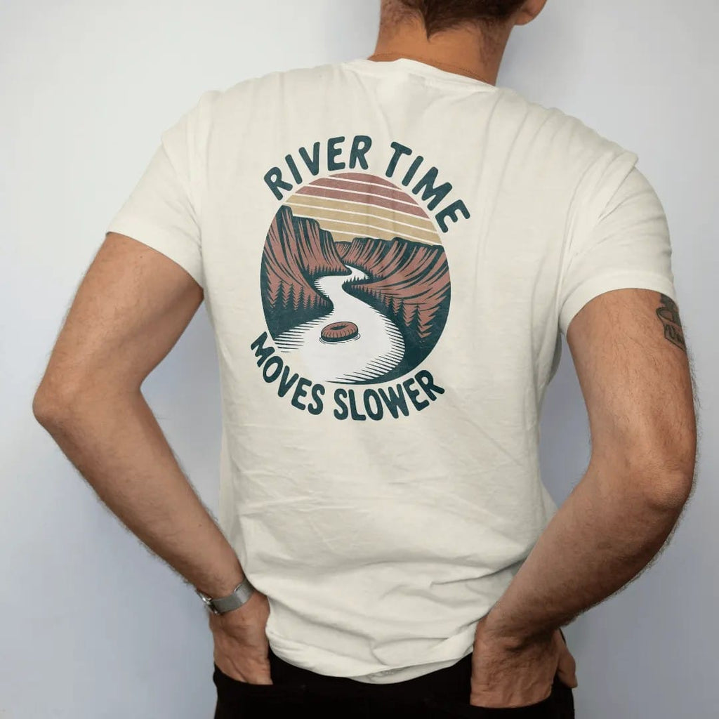 Man wearing a Ivory tee, seen from the back: a slow winding river through a canyon with a lone tube floater, wavy text following the river, faded 70s park-souvenir style, lettered "RIVER TIME / MOVES SLOWER" in chunky rounded 70s serif letters with…