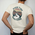 Man wearing a Ivory tee, seen from the back: a slow winding river through a canyon with a lone tube floater, wavy text following the river, faded 70s park-souvenir style, lettered "RIVER TIME / MOVES SLOWER" in chunky rounded 70s serif letters with…
