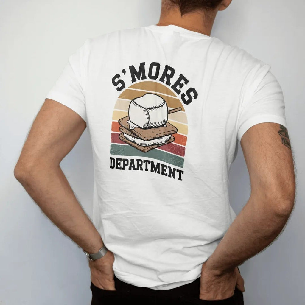 Man wearing a White tee, seen from the back: a toasted marshmallow on a stick dripping between graham crackers, official-department seal layout, faded 70s park-souvenir style, lettered "S'MORES / DEPARTMENT" in chunky rounded 70s serif letters with…