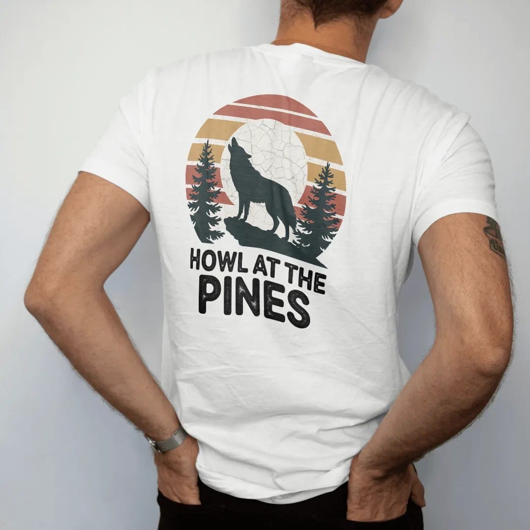 Man wearing a White tee, seen from the back: a wolf howling on a rocky ledge with a full moon behind it and pines in silhouette, faded 70s park-souvenir style, lettered "HOWL AT THE PINES" in chunky rounded 70s letters with a drop shadow, printed…