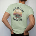 Man wearing a Light Green tee, seen from the back: a small dome tent under a cartoon rain cloud with a sun peeking out behind it, raindrops and puddles, faded 70s park-souvenir style, lettered "RAIN OR SHINE / CAMP ANYWAY" in chunky rounded 70s…