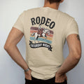 Man wearing a Sandstone tee, seen from the back: vintage rodeo poster layout with a bucking bronco and rider, "RODEO" in huge chunky 70s slab letters above and "SATURDAY NIGHT" on a banner below, in a faded 1970s souvenir style with a worn…