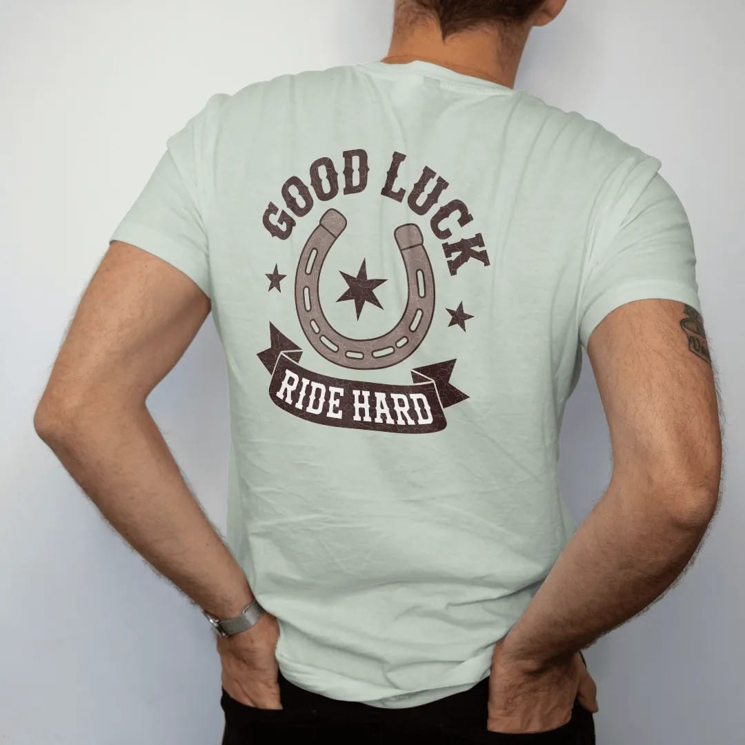 Man wearing a Bay tee, seen from the back: a worn horseshoe with nail holes framing a small eight-point star, "GOOD LUCK" arched above in chunky 70s block letters and "RIDE HARD" on a ribbon below, in a faded 1970s souvenir style with a worn…