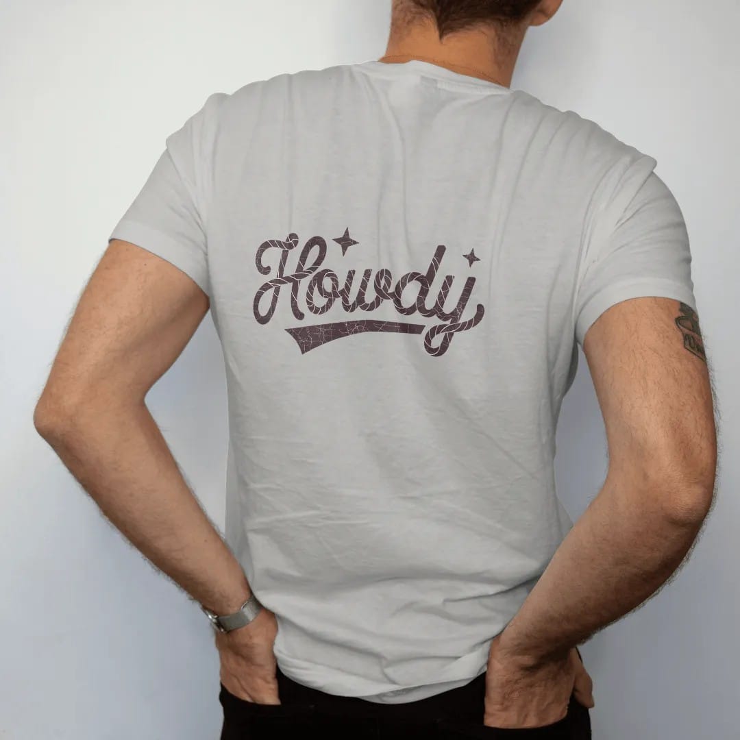 Man wearing a Granite tee, seen from the back: the word "HOWDY" written in a looping 70s rope script with a coiled rope end and a small star on each side, in a faded 1970s souvenir style with a worn cracked-ink texture, printed in saddle brown,…