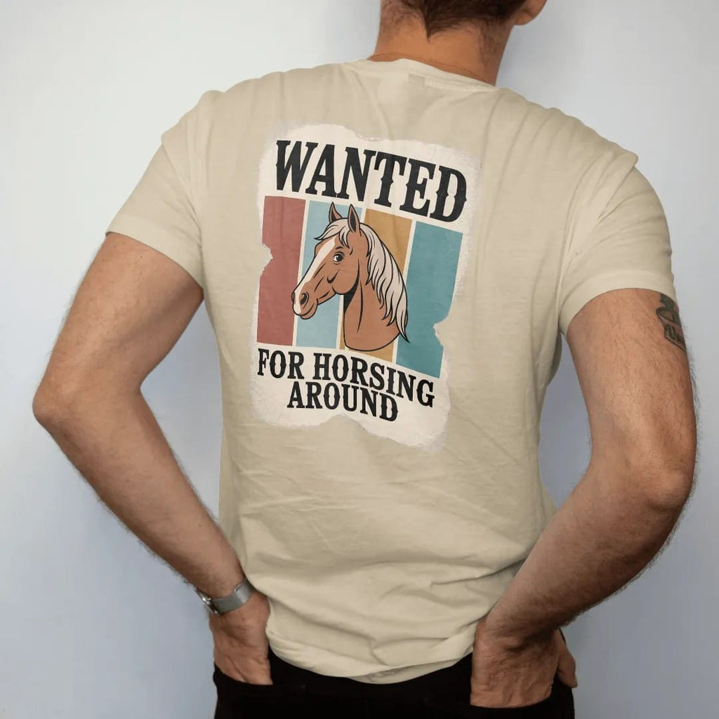 Man wearing a Sandstone tee, seen from the back: an old torn wanted poster with a cartoon horse portrait in the center, "WANTED" in chunky 70s slab letters at top and "FOR HORSING AROUND" in small caps below, in a faded 1970s souvenir style with a…