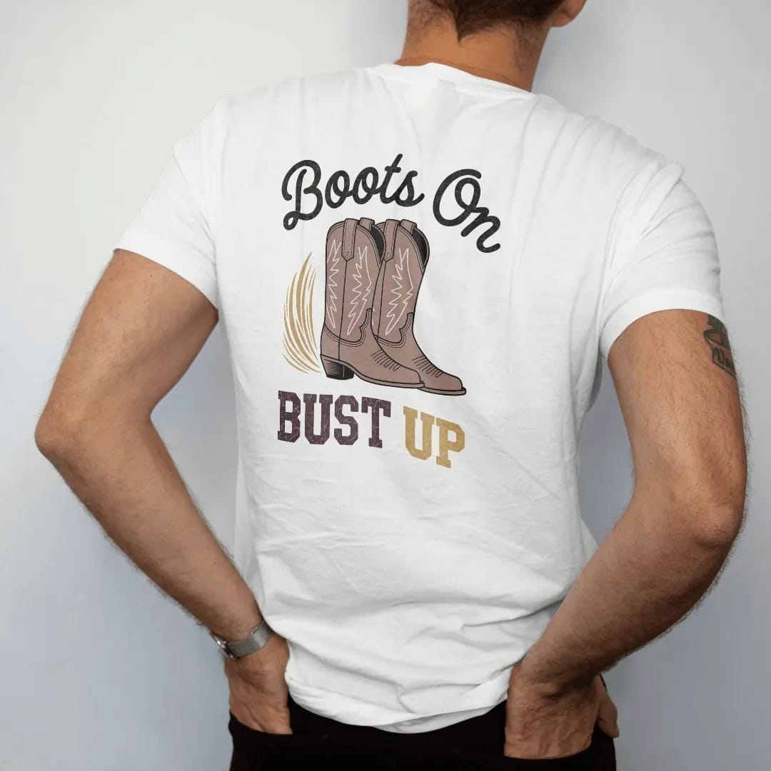 Man wearing a White tee, seen from the back: a pair of worn cowboy boots with stitched shafts kicking up a puff of dust, "BOOTS ON" in a looping 70s rope script above and "DUST UP" in chunky 70s block letters below, in a faded 1970s souvenir style…