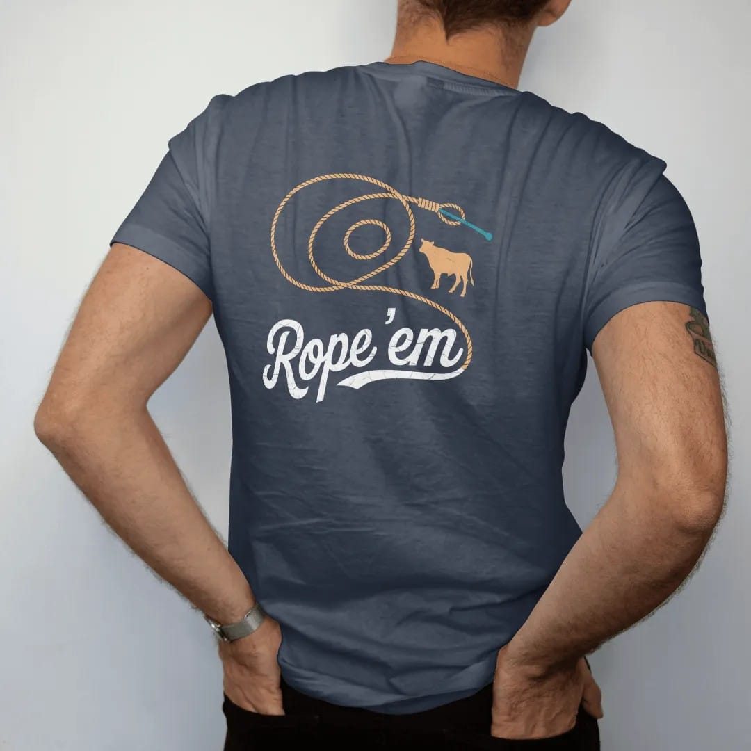 Man wearing a Midnight tee, seen from the back: a coiled lasso flying open into a big loop with a small calf silhouette, "ROPE 'EM" in a looping 70s rope script across the loop, in a faded 1970s souvenir style with a worn cracked-ink texture,…