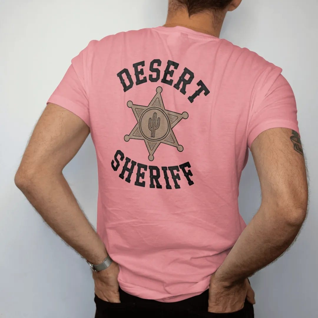 Man wearing a Watermelon tee, seen from the back: a worn six-point sheriff star badge with a small cactus engraved in the center, "DESERT" in chunky 70s slab letters above and "SHERIFF" in chunky 70s block letters below, in a faded 1970s souvenir…